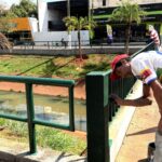 Trabalhador de boné vermelho pinta de verde o guarda-corpo de uma ponte sobre o canal da Avenida Aurora, em Olímpia