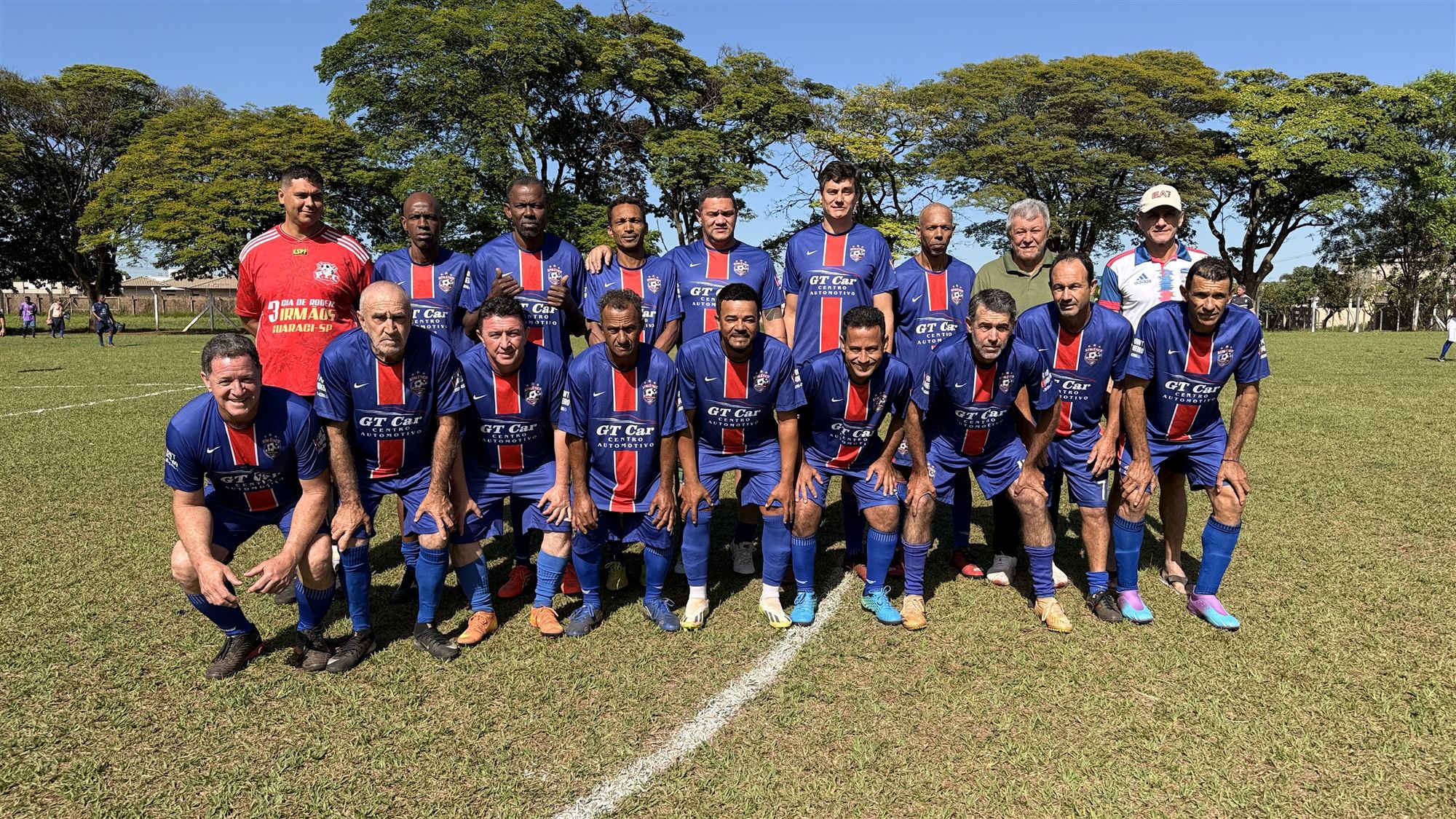 Equipe de camisas azuis com faixa vermelha posa para foto no campo antes de partida do Campeonato Veterano de Futebol de Olímpia