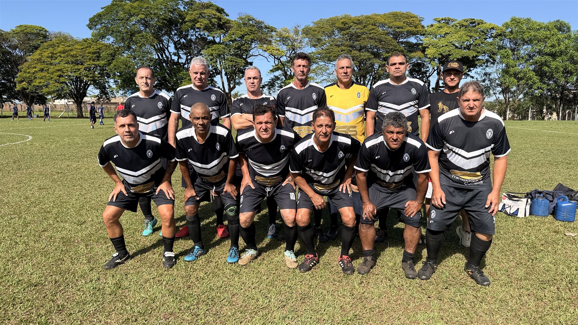 Equipe de camisas pretas com listras brancas posa para foto antes de partida do Campeonato Veterano de Futebol de Olímpia