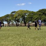 Jogadores de camisas azul e preta disputam a bola em campo de grama durante partida do Campeonato Veterano de Futebol de Olímpia