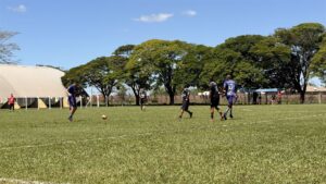 Jogadores de camisas azul e preta disputam a bola em campo de grama durante partida do Campeonato Veterano de Futebol de Olímpia