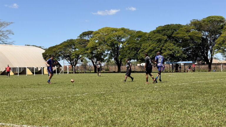 Jogadores de camisas azul e preta disputam a bola em campo de grama durante partida do Campeonato Veterano de Futebol de Olímpia