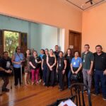 Integrantes do Conselho Municipal dos Direitos da Pessoa com Deficiência de Olímpia reunidos em sala com piso de madeira