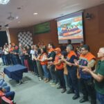 Participantes de treinamento da Defesa Civil em um auditório, em pé e aplaudindo, com telão da Operação El Niño ao fundo