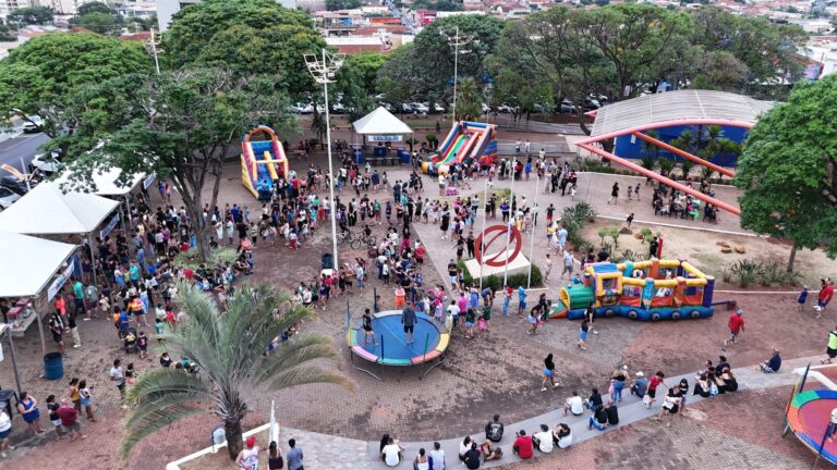 Vista aérea de praça de Olímpia com brinquedos infláveis, cama elástica e famílias reunidas em evento para crianças