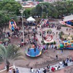 Vista aérea de praça de Olímpia com brinquedos infláveis, cama elástica e famílias reunidas em evento para crianças