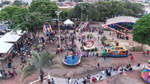 Vista aérea de praça de Olímpia com brinquedos infláveis, cama elástica e famílias reunidas em evento para crianças