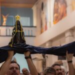 Imagem de Nossa Senhora Aparecida erguida sobre um manto azul, carregado por fiéis, no Santuário de Olímpia