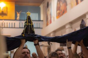 Imagem de Nossa Senhora Aparecida erguida sobre um manto azul, carregado por fiéis, no Santuário de Olímpia