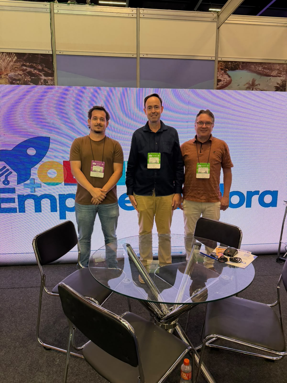 Três homens posam diante do painel Olímpia Empreendedora, dentro do estande de Olímpia na Feira do Empreendedor 2026