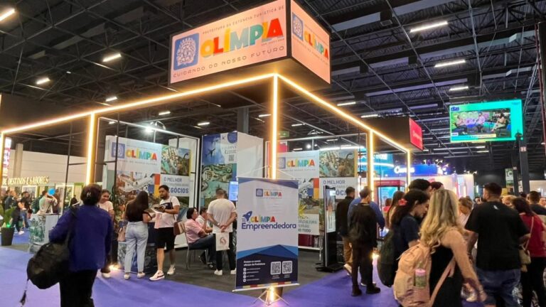 Estande de Olímpia em edição anterior da Feira do Empreendedor, com banner do programa Olímpia Empreendedora e visitantes conversando