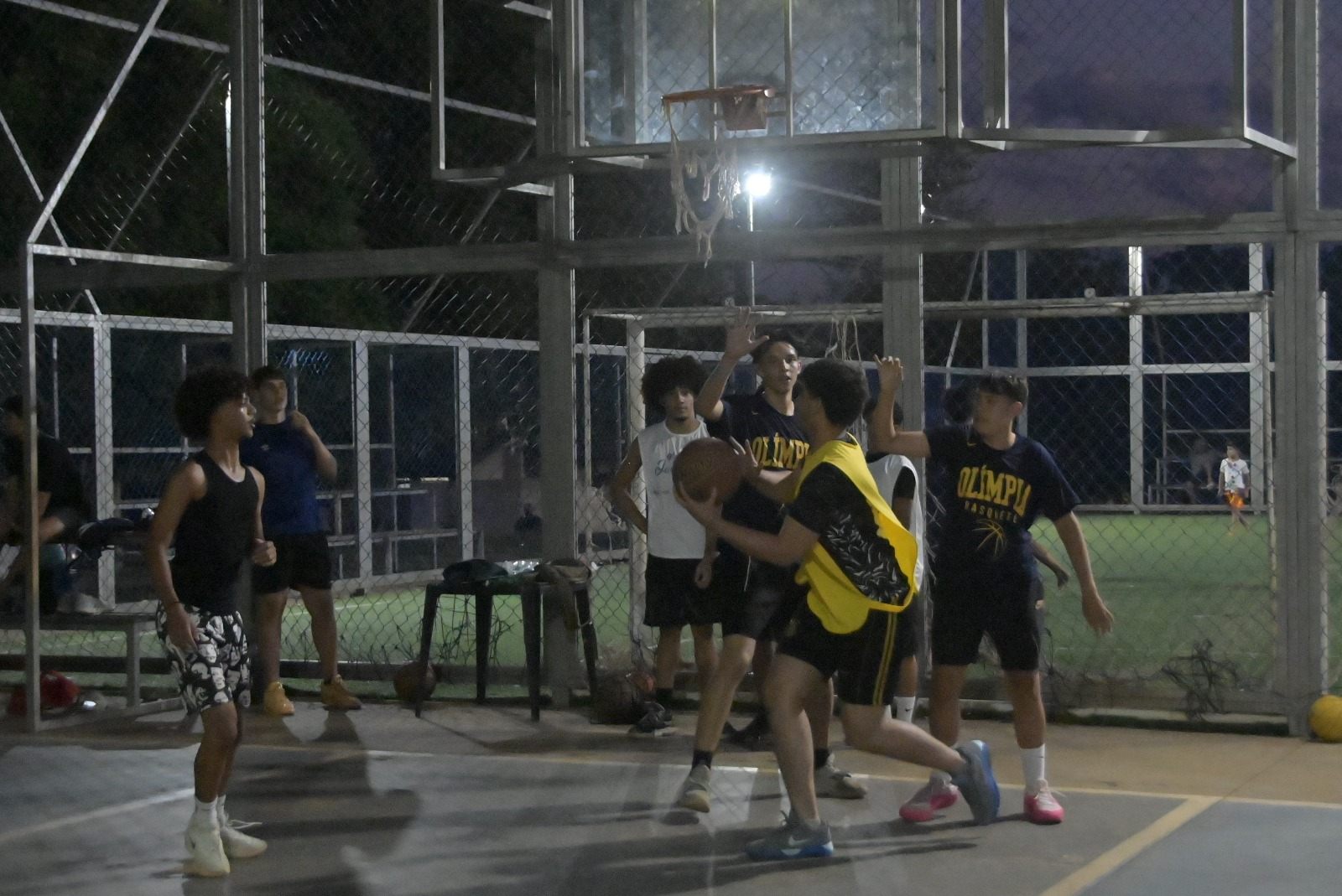 Jovens disputam partida de basquete em quadra iluminada, à noite