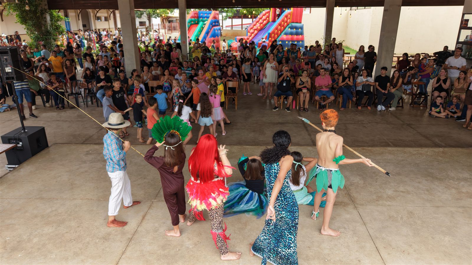 Crianças fantasiadas encenam peça de teatro no palco da Lancheria, diante de plateia sentada