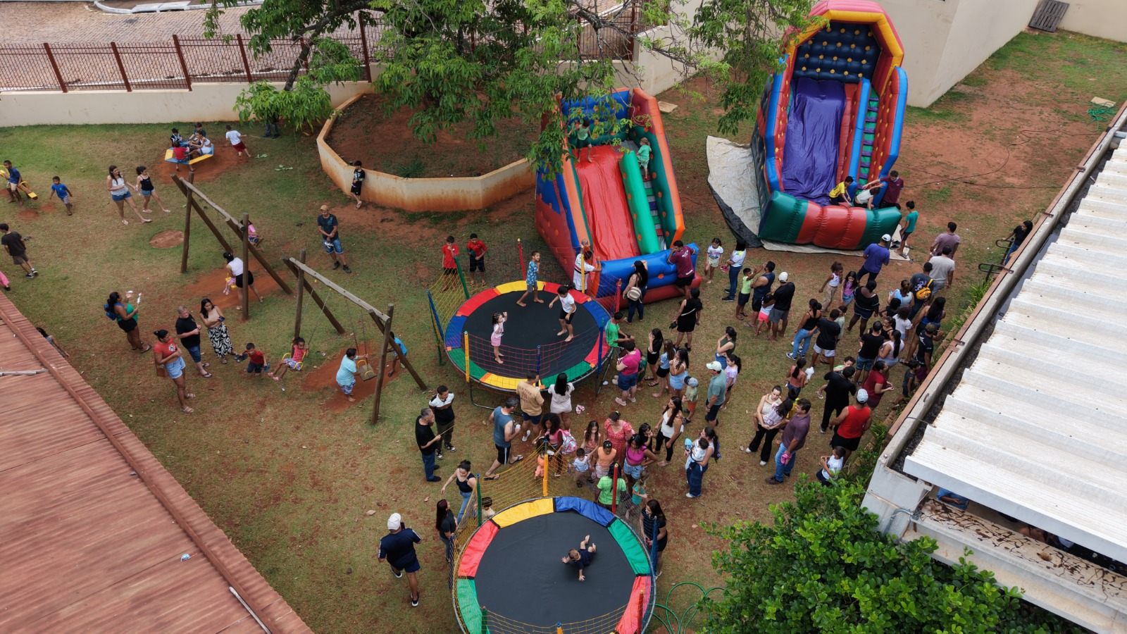 Vista aérea de crianças e famílias em cama elástica, balanços e brinquedos infláveis nos jardins da ECO