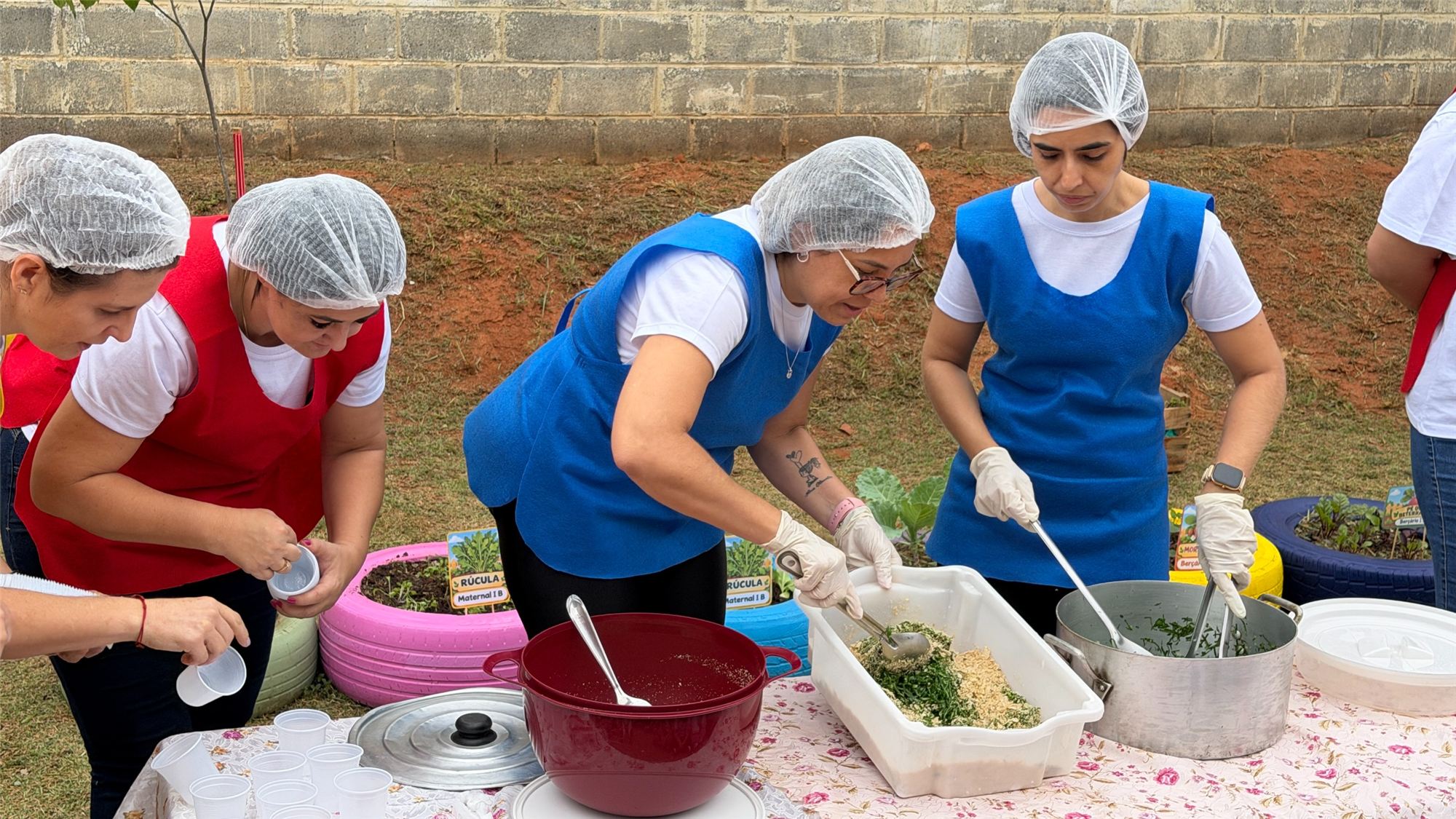 Profissionais da escola, de toucas descartáveis, preparam e servem farofa de couve em uma mesa ao ar livre