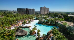 Vista aérea do Hot Beach, em Olímpia, com a praia artificial, piscinas, palmeiras e os prédios dos resorts ao fundo