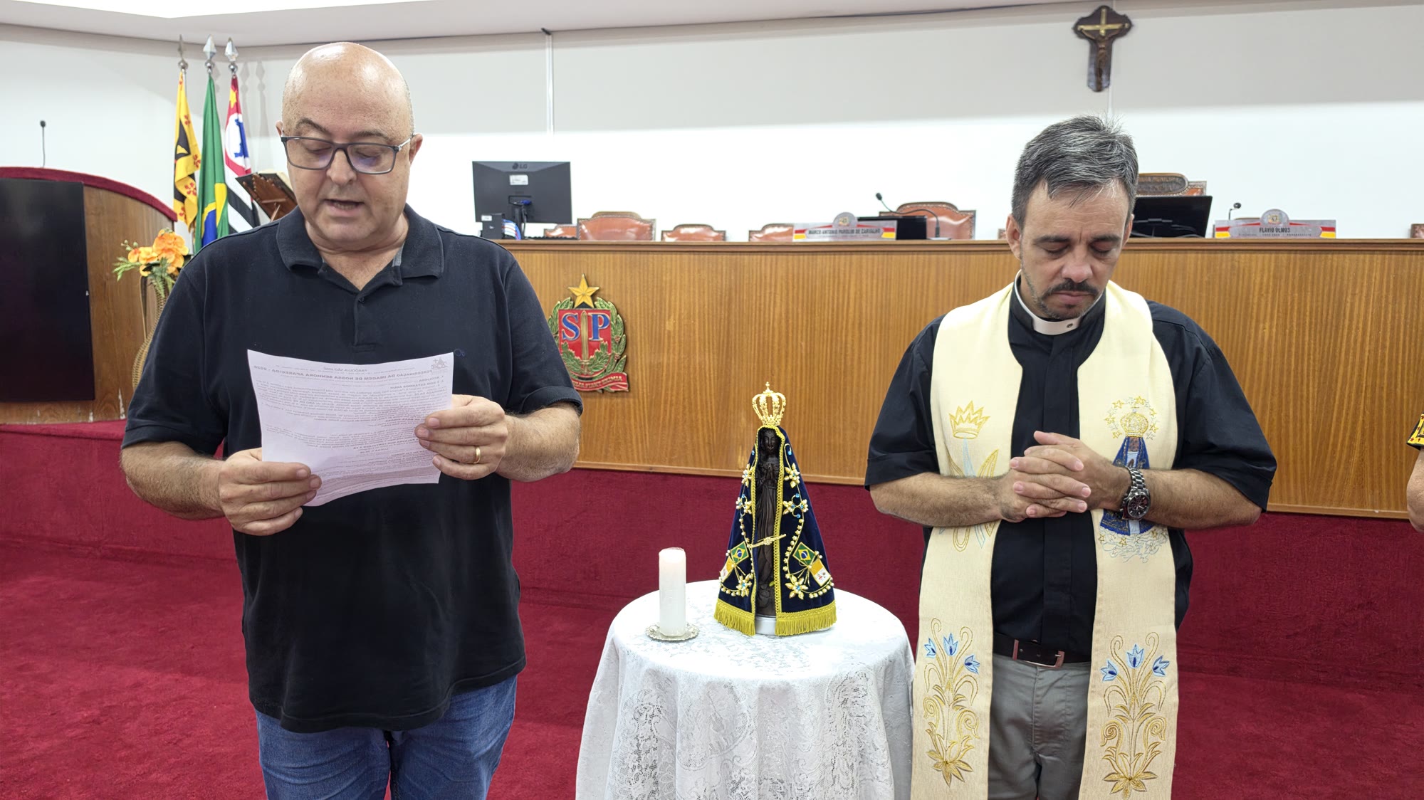 Padre e participante durante momento de oração diante da imagem de Nossa Senhora Aparecida na Câmara de Olímpia