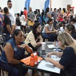Candidatos conversam com recrutadores em mesas de atendimento, com público ao fundo, durante mutirão de emprego em Olímpia