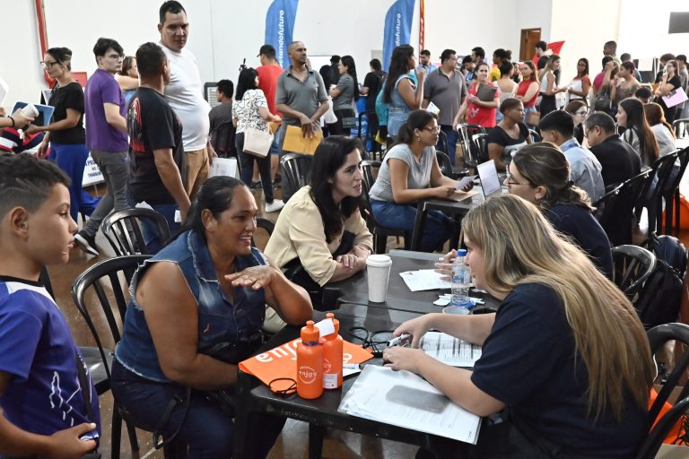 Candidatos conversam com recrutadores em mesas de atendimento, com público ao fundo, durante mutirão de emprego em Olímpia