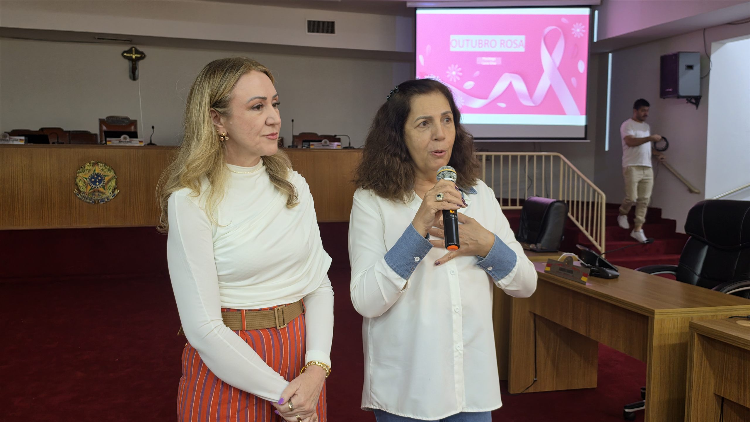 Duas mulheres no plenário da Câmara Municipal de Olímpia, uma delas falando ao microfone, antes da palestra do Outubro Rosa