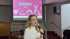 Palestrante fala ao microfone diante de telão do Outubro Rosa no plenário da Câmara Municipal de Olímpia
