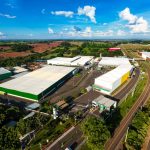 Vista aérea do complexo industrial da Bebidas Poty, em Potirendaba, com galpões brancos e verdes cercados por áreas de lavoura