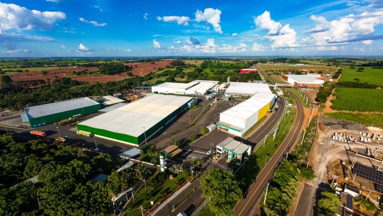 Vista aérea do complexo industrial da Bebidas Poty, em Potirendaba, com galpões brancos e verdes cercados por áreas de lavoura