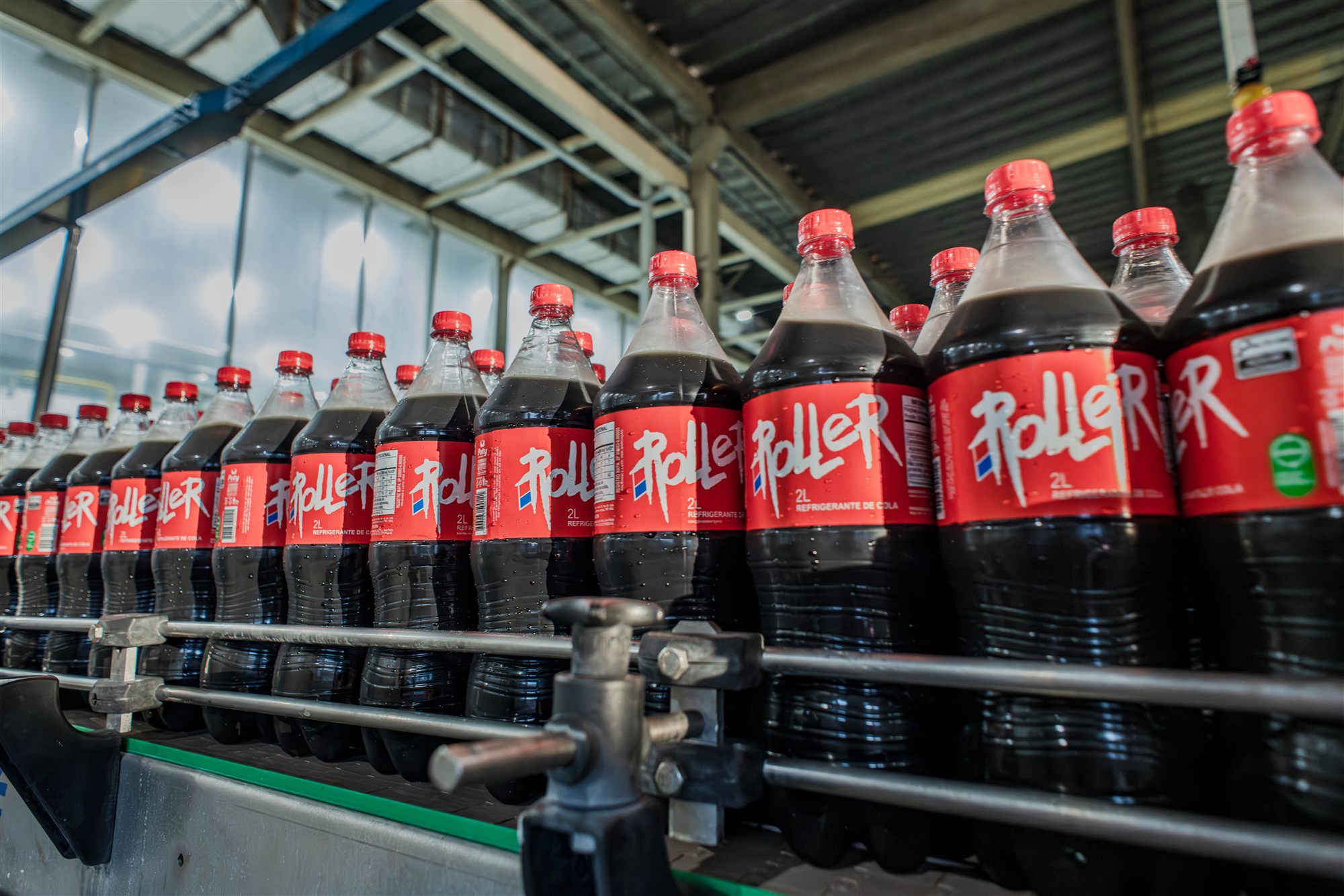 Garrafas de refrigerante de cola de 2 litros alinhadas em esteira na linha de produção da Poty