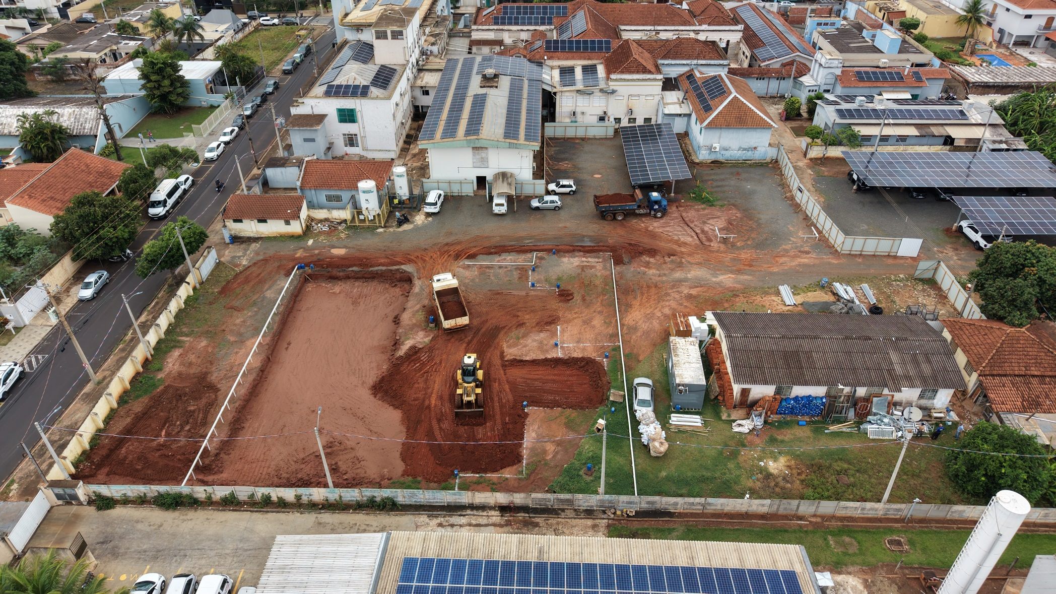 Vista aérea do canteiro de obras da nova ala da Santa Casa de Olímpia, com caminhão e pá-carregadeira movimentando terra vermelha