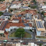 Vista aérea da Santa Casa de Olímpia com telhados de placas solares e, ao fundo, o terreno em obras da nova ala