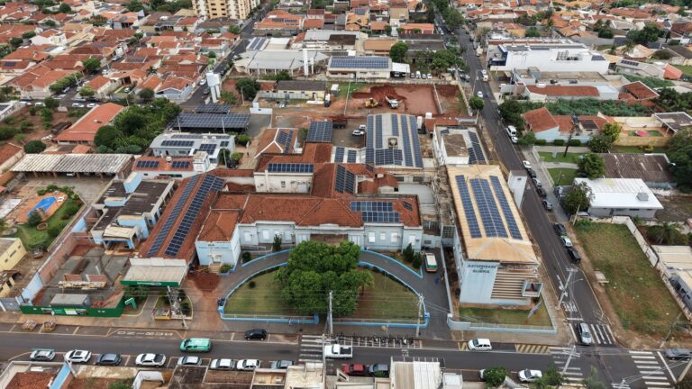 Vista aérea da Santa Casa de Olímpia com telhados de placas solares e, ao fundo, o terreno em obras da nova ala