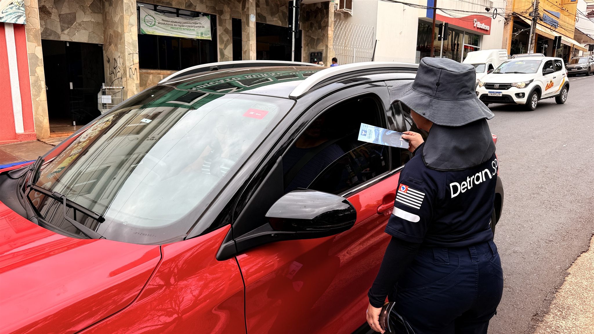 Agente do Detran-SP entrega panfleto a motorista durante ação de conscientização no Centro de Olímpia