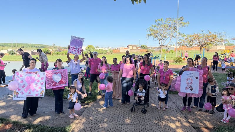 Grupo de adultos e crianças vestidos de rosa, com cartazes e balões, ao ar livre durante ação do Talento Rosa