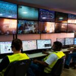 Operadores de uniforme acompanham telas de monitoramento em sala de controle de usina