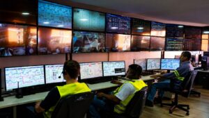 Operadores de uniforme acompanham telas de monitoramento em sala de controle de usina