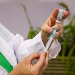 Profissional de saúde prepara dose de vacina, enchendo a seringa a partir do frasco