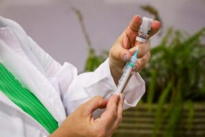 Profissional de saúde prepara dose de vacina, enchendo a seringa a partir do frasco